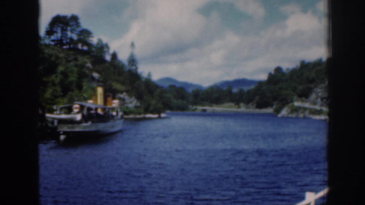 Small boat on a broad river with wooded banks and distant hills.