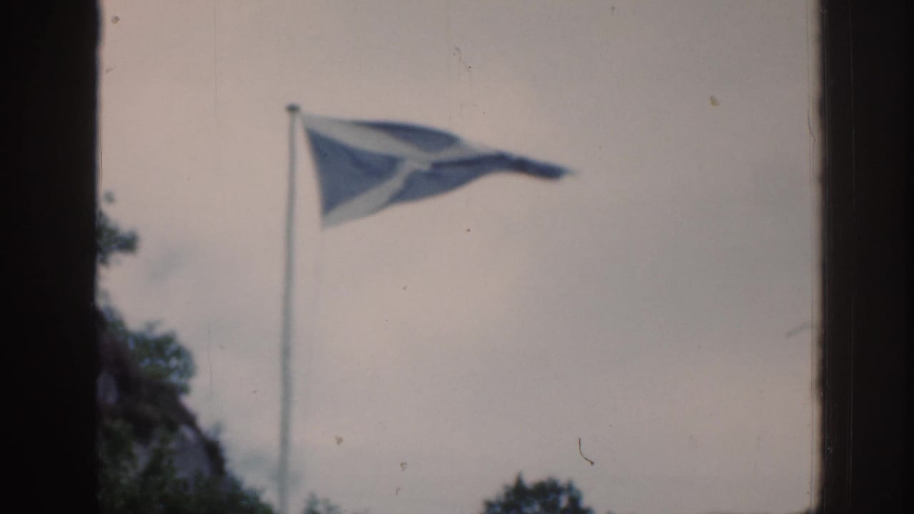 Scottish flag waving on a pole beside dark window framing and an overcast sky.