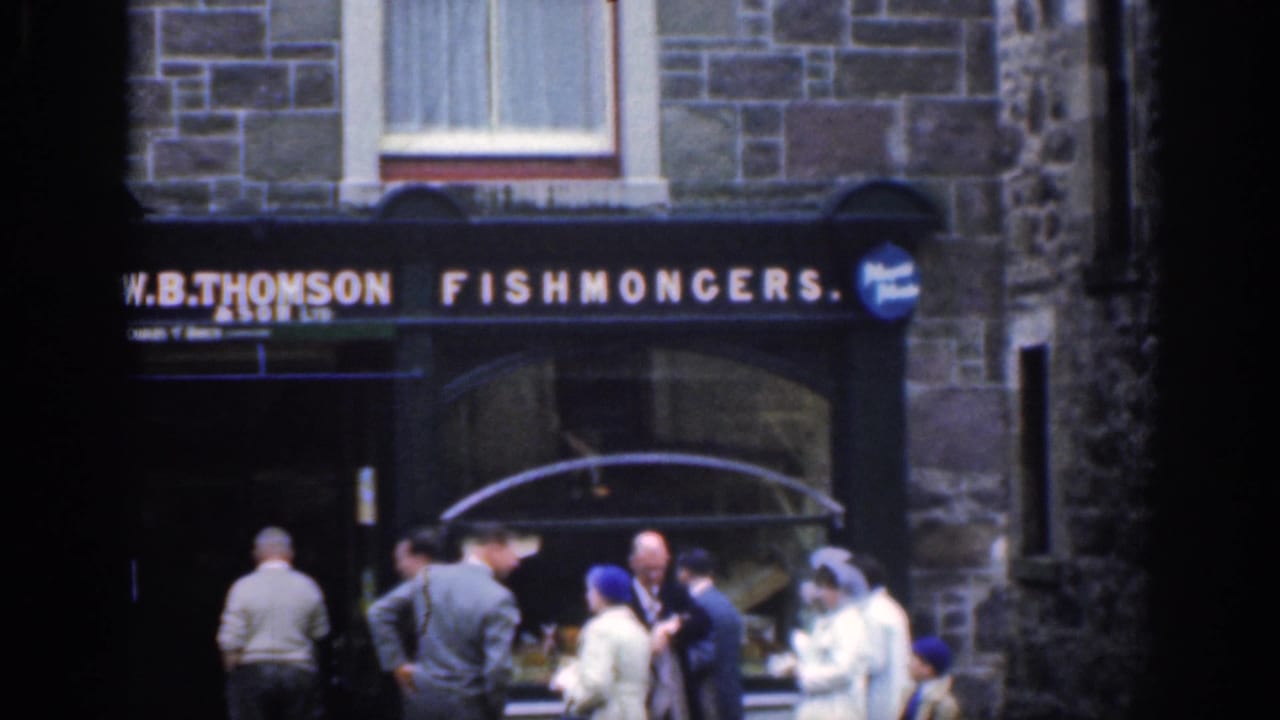 People gathered outside a stone fishmongers shop with a W.B. Thomson sign.