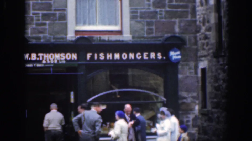 1961 Scotland home-movie frame showing pedestrians outside a stone storefront marked W.B. Thomson Fishmongers.