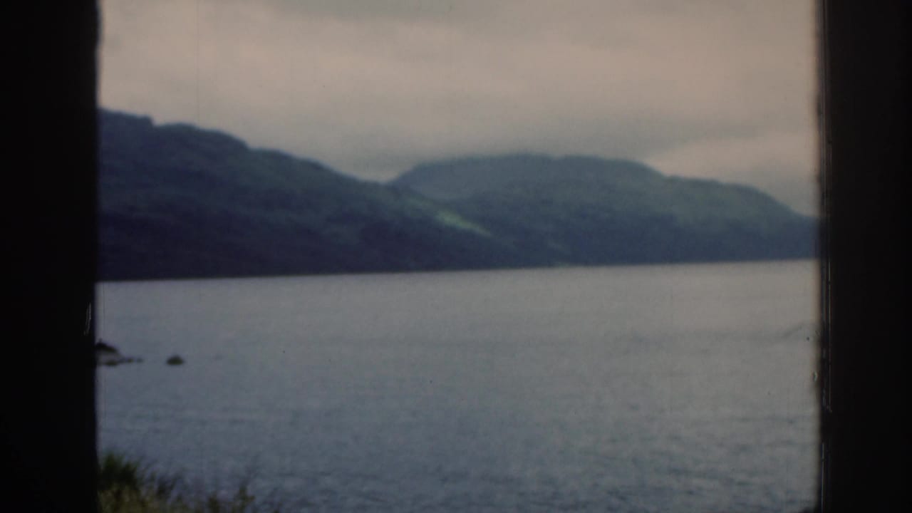 Calm loch and distant hills seen through a dark window frame.