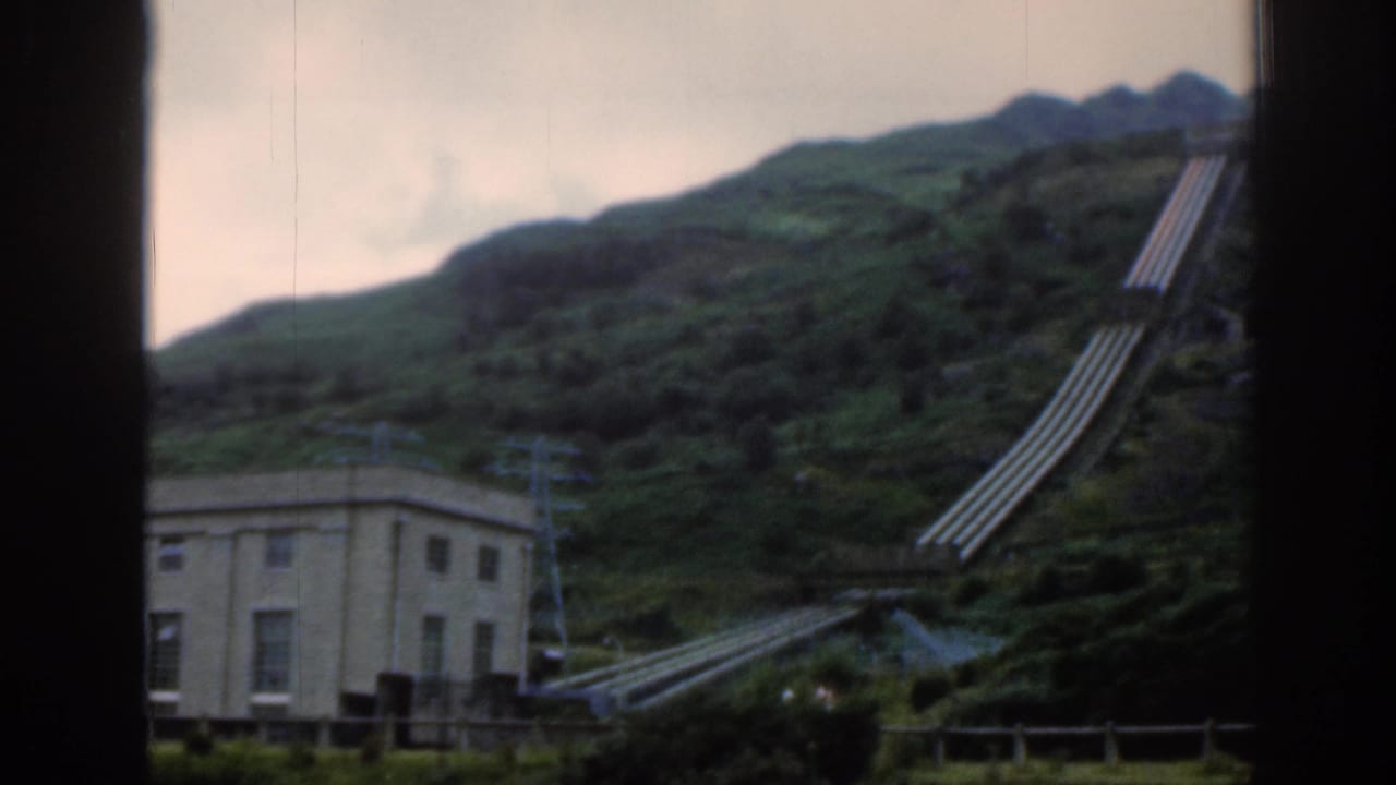Hillside power station building with pipes running up a green slope.