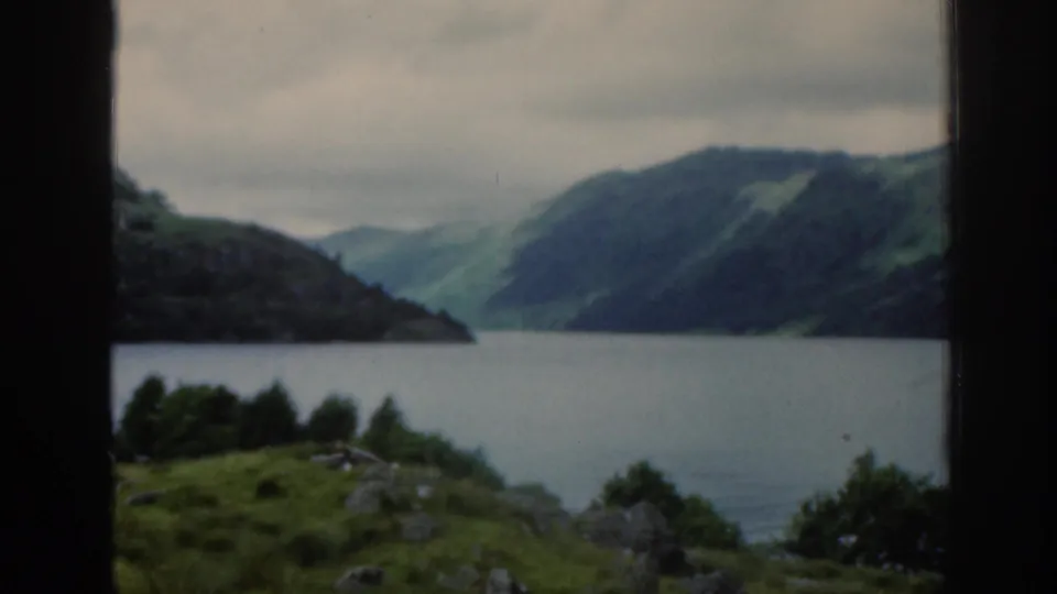 A wide 1961 Scotland travel view shows a loch bordered by green hills, rocky foreground, trees, and misty mountains under an overcast sky.