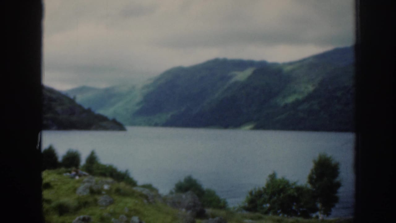 Calm lake seen through dark vertical window bars with green hills under an overcast sky.