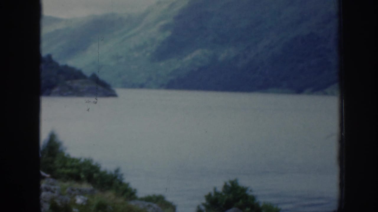 Large lake and green mountains seen through a dark window-like frame.