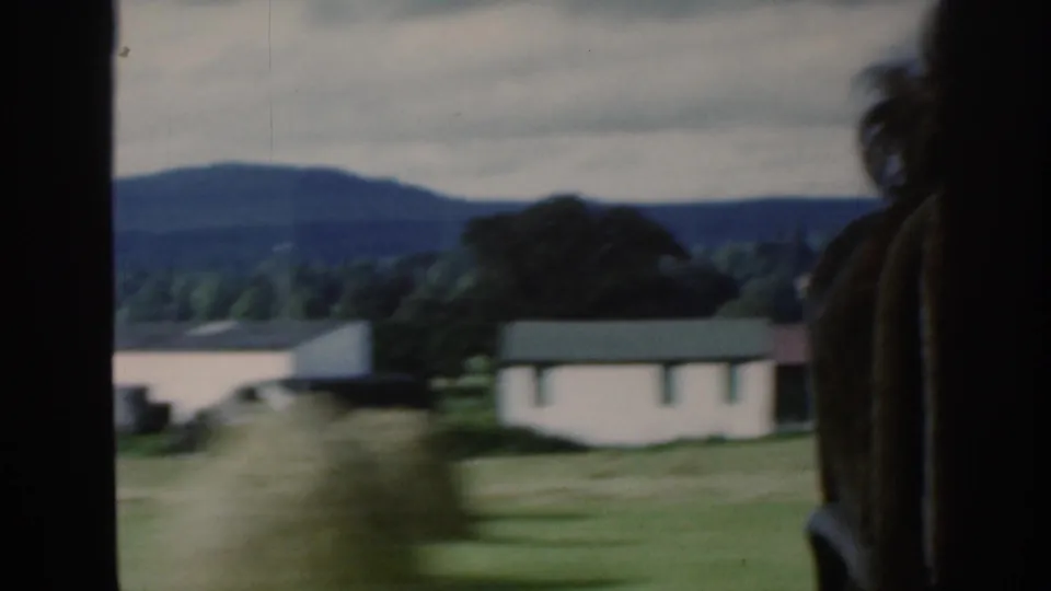 The final 1961 Scotland frame shows a white rural building, distant hills, overcast sky, and a partial passenger figure by the window.
