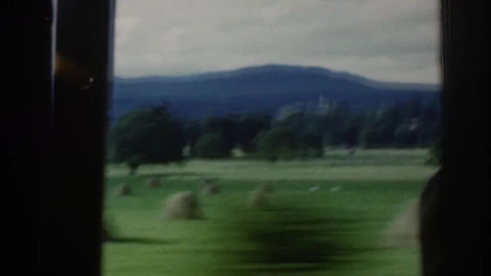 Soft 8mm view of Scottish countryside through a window, with pasture, hay bales, trees, and blue-gray hills.