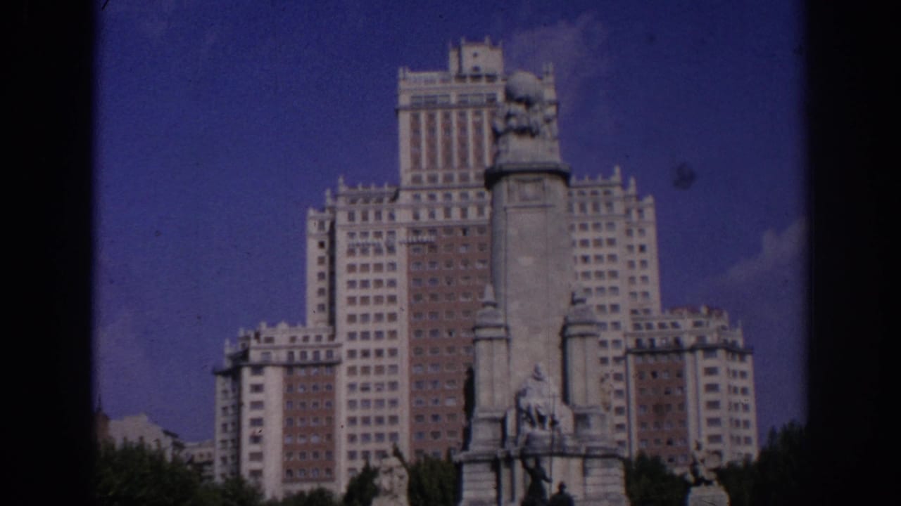 Wide view of a stone monument in front of Edificio España under a blue sky.