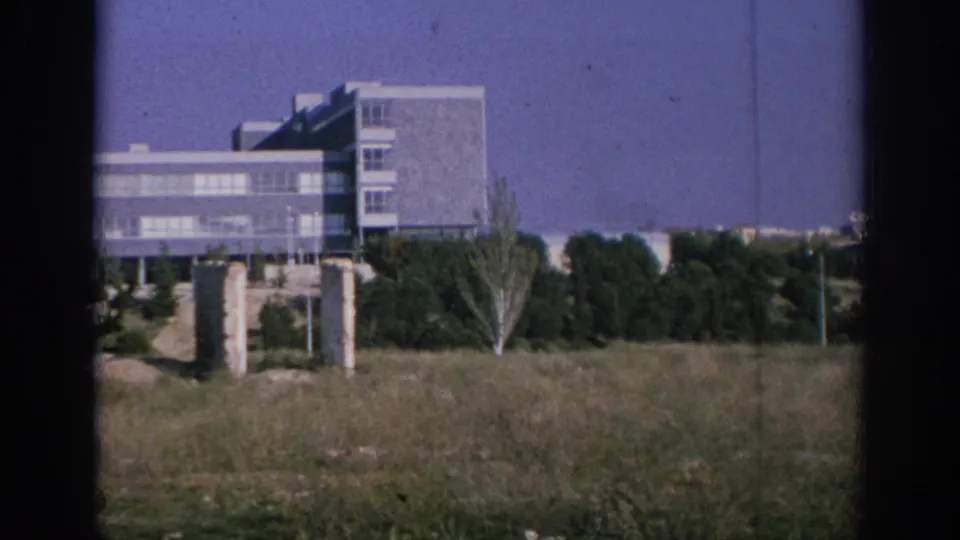 Spain 1966 8mm frame showing a gray modernist building across open grass, with trees and film gate shadows at the sides.