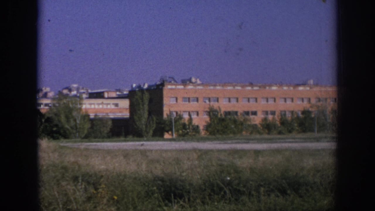 Long red brick building behind grass and trees under a purple-blue sky.