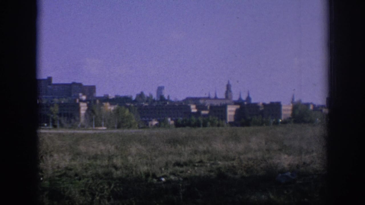 1966 Spain 8mm frame showing an overgrown field, distant rooftops and spires, and heavy dark borders from a window or film gate.