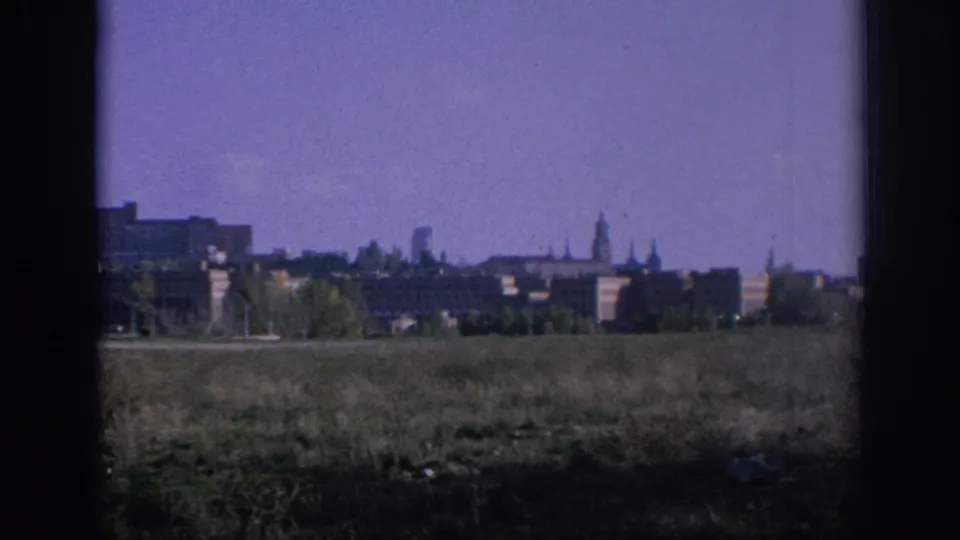 1966 Spain 8mm frame showing an overgrown field, distant rooftops and spires, and heavy dark borders from a window or film gate.