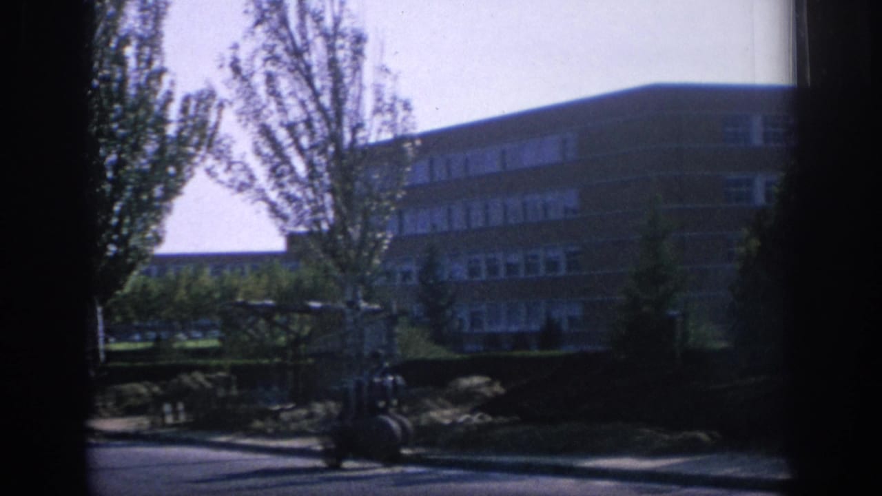 Brick apartment building partly obscured by dark vertical framing and trees.
