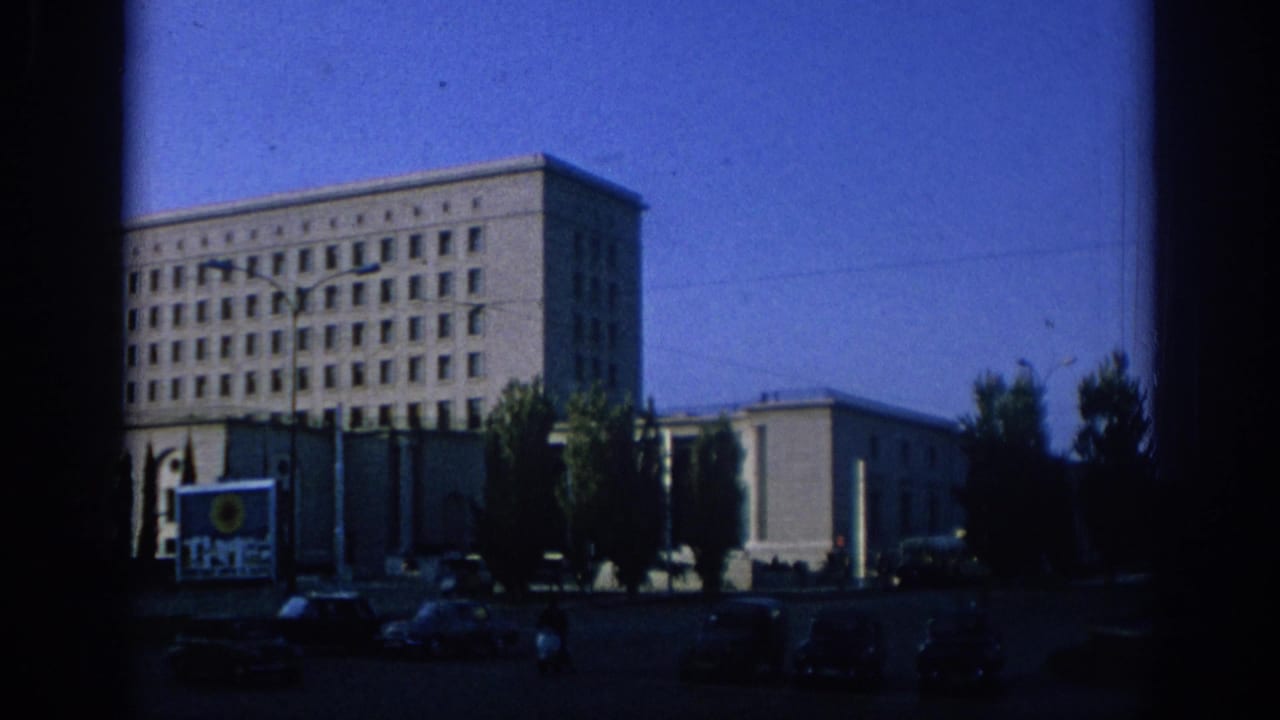 1966 Spain street view with a large institutional-looking building, parked and moving cars, trees, and visible signage.