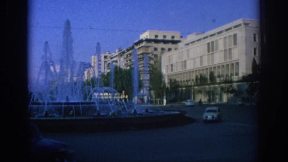 1966 Spain city view with a fountain in the foreground, public buildings, street paving, and a light-colored car crossing the square.
