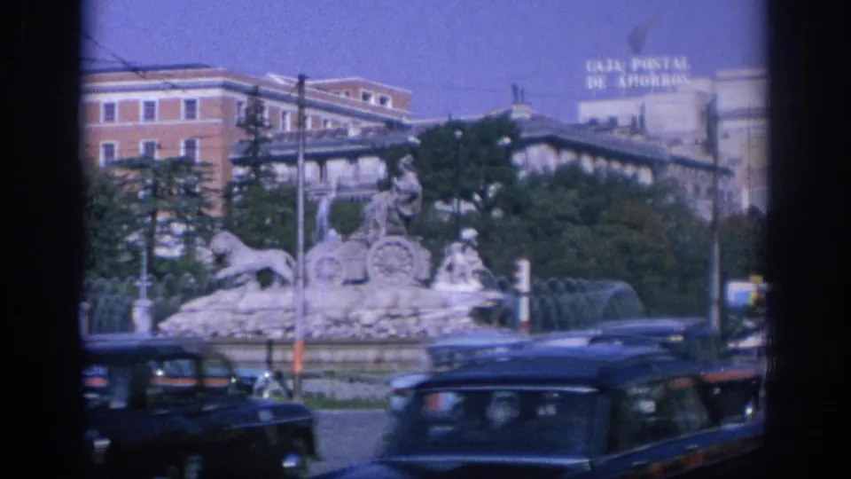 A sculpted fountain with horses and figures stands before traffic, with a visible Caja Postal de Ahorros sign in the background.