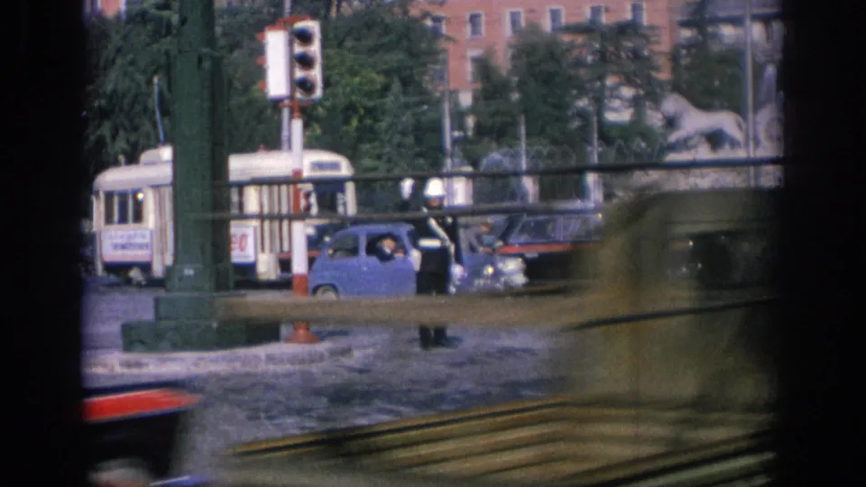 1966 Spain traffic view with a signal pole, a bus or tram, small blue car, officer area, and sculptural fountain beyond the street.