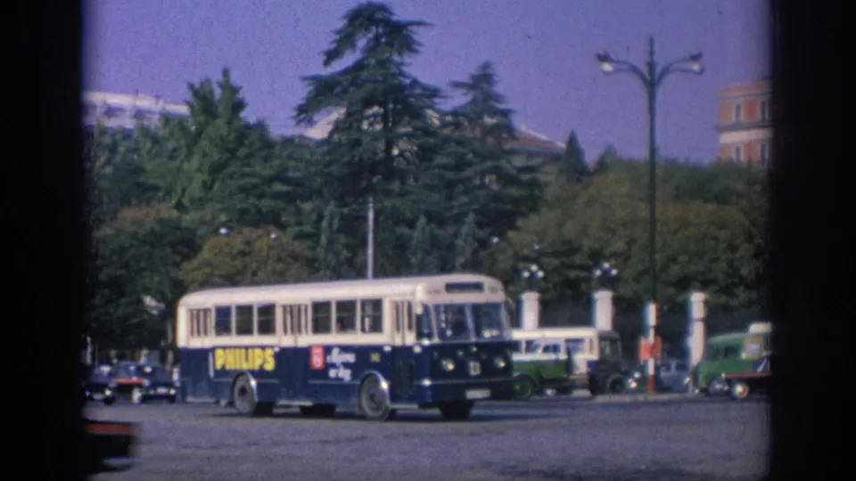 1966 Spain urban traffic view with a Philips-branded bus, green vehicle, parked or moving cars, trees, and tall streetlamps.