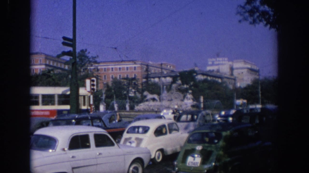Street traffic with a red-and-white bus passing near compact cars and a fountain.