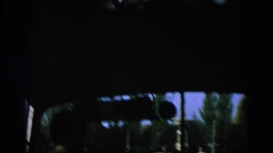 Inside-car 1966 Spain travel frame with dark vehicle interior, mirror silhouette, trees, street signs, and motion-softened roadside details.