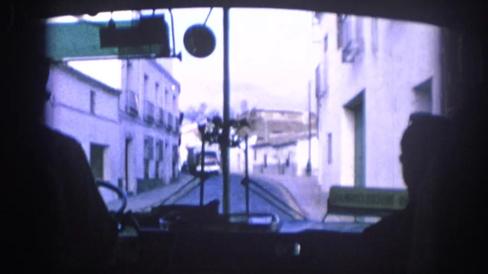 1966 Spain bus interior view looking through the windshield at white buildings along a narrow town street.