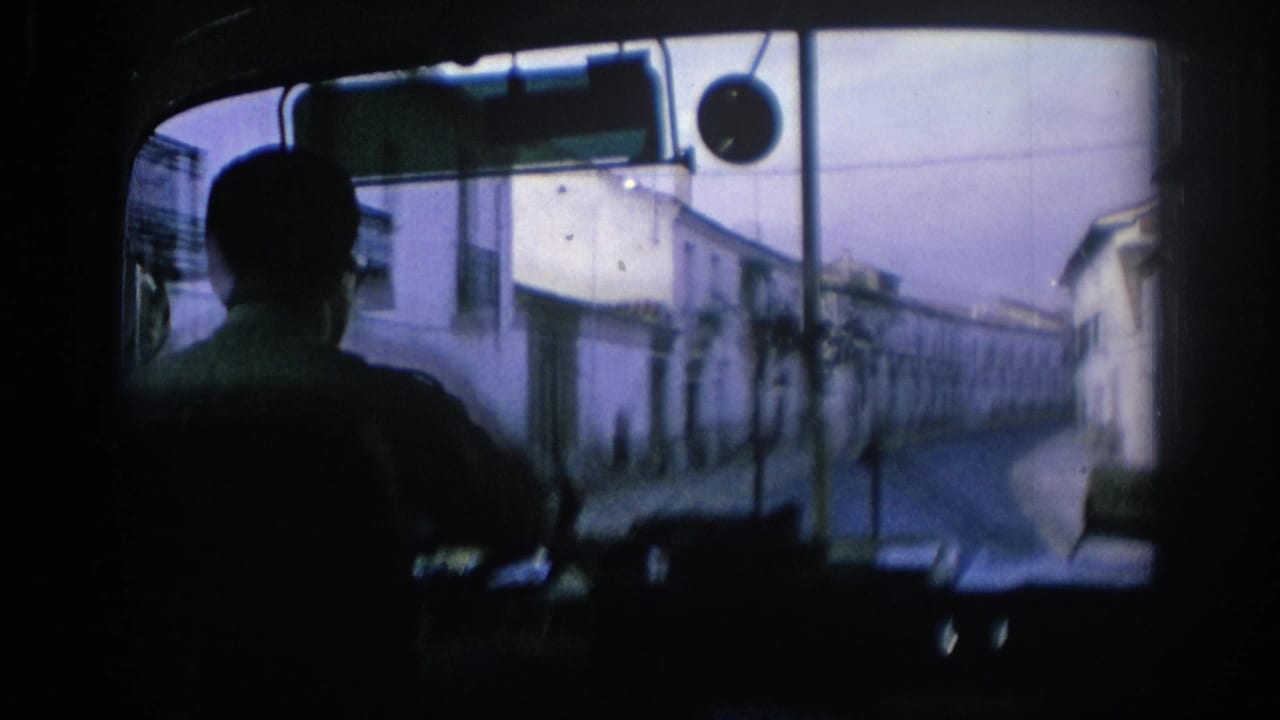 Silhouetted bus driver seen from behind through a front window on a narrow street.