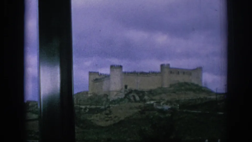 1966 Spain 8mm view of a medieval-looking castle on a hill, partly bordered by the bus window interior.