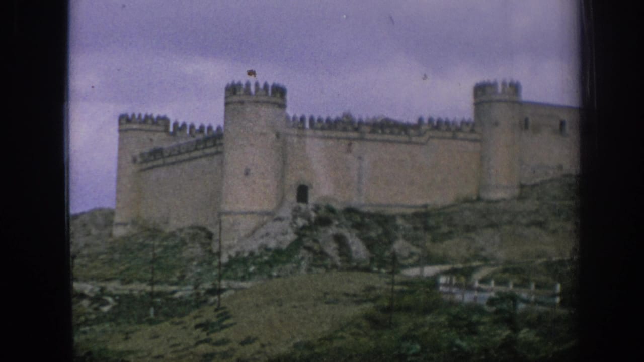 1966 Spain 8mm frame showing a medieval-style stone castle with towers and battlements on a rocky grassy slope.