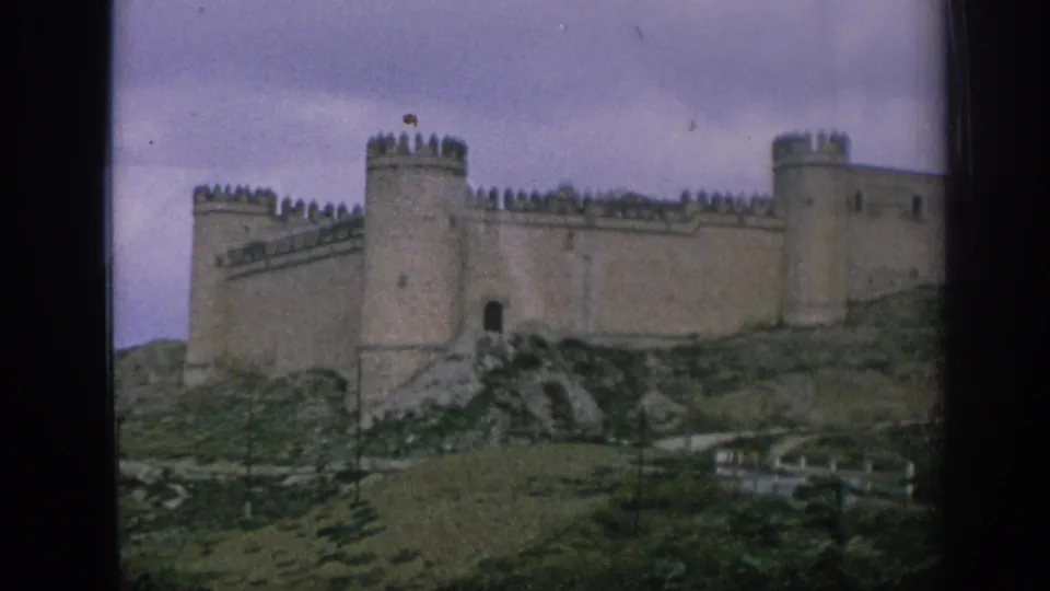 1966 Spain 8mm frame showing a medieval-style stone castle with towers and battlements on a rocky grassy slope.