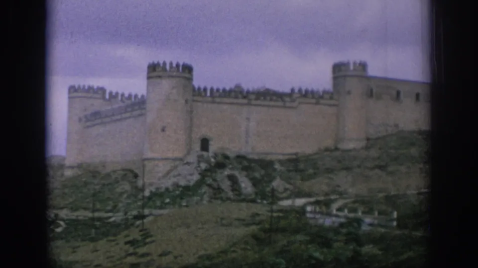 1966 Spain home-movie frame of a hilltop castle exterior, with battlements, towers, and a dark entrance visible.
