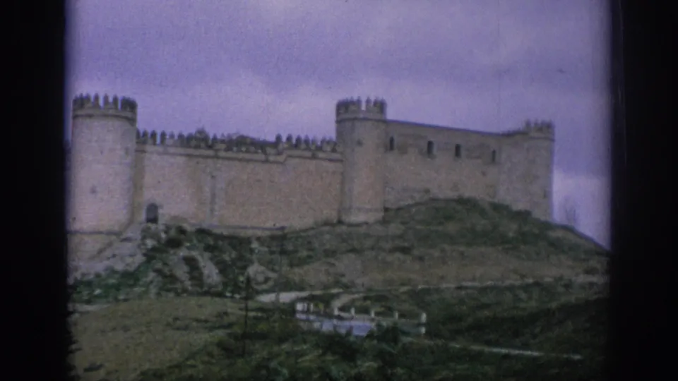 1966 Spain travel footage frame showing the castle exterior across the hill, with faded color and visible 8mm frame borders.