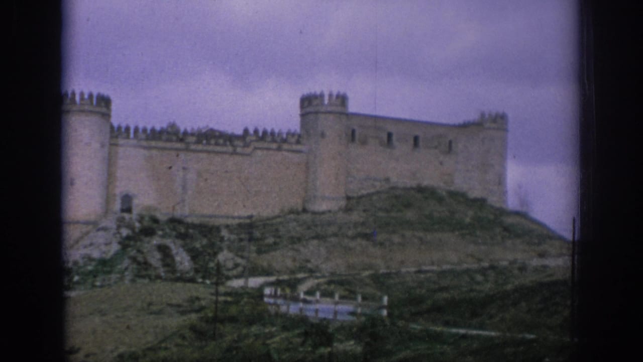 1966 Spain 8mm frame showing a distant hilltop stone castle with crenellated walls, round towers, and dark film borders.