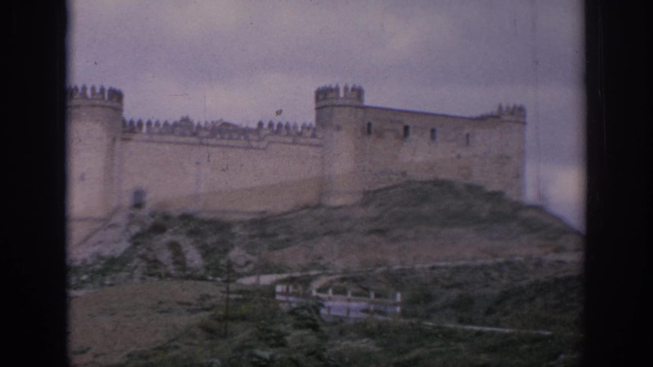 Crenellated stone castle on a grassy hillside under an overcast sky.
