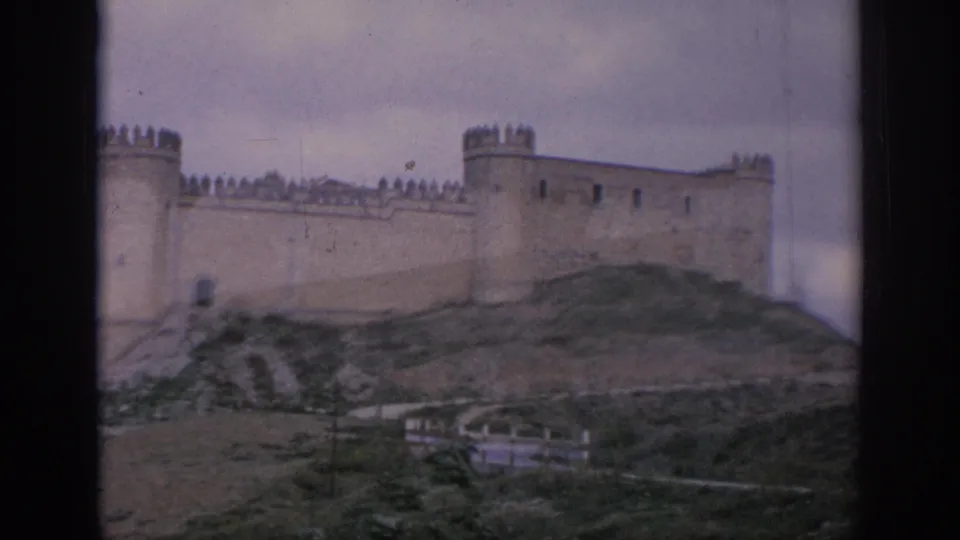 1966 Spain 8mm frame showing a stone castle with towers and crenellated walls above a grassy hillside.