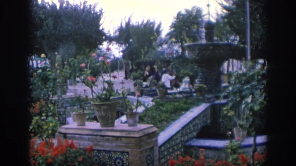 1966 Spain garden view with tiled terraces, potted plants, red flowers, a fountain, and visitors seated or standing in the distance.