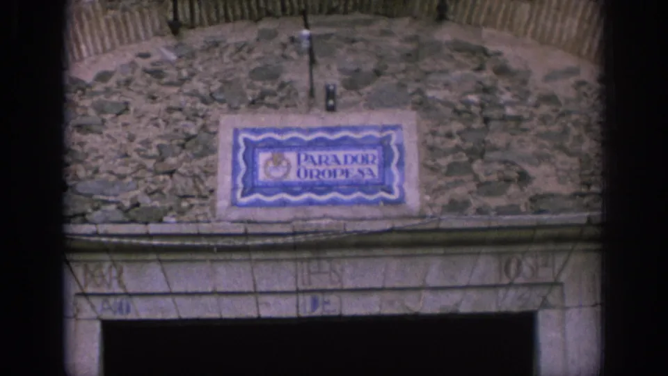 1966 Spain 8mm frame showing a blue and white Parador Oropesa ceramic sign set into a rough stone wall above an arched entrance.