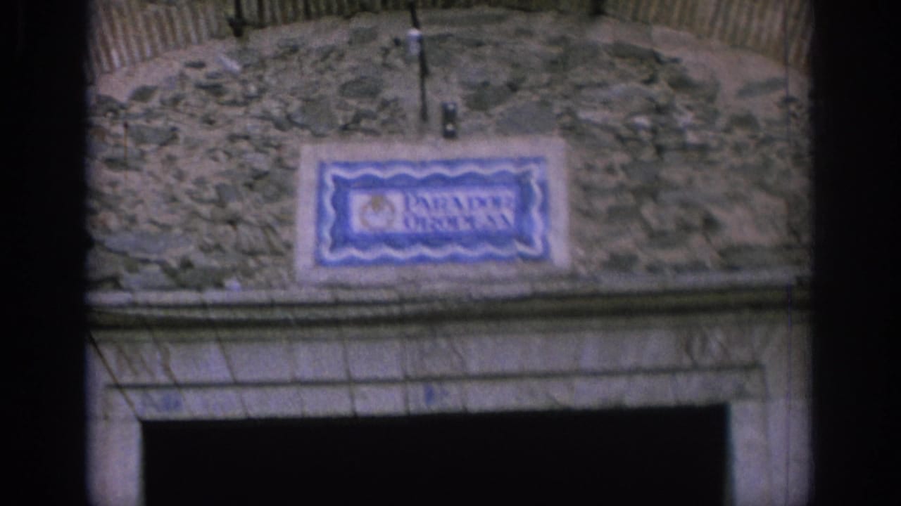 Vintage 8mm view in Spain of the Parador Oropesa sign on a weathered stone wall, framed closely above a dark entry opening.