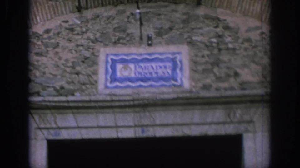 Vintage 8mm view in Spain of the Parador Oropesa sign on a weathered stone wall, framed closely above a dark entry opening.