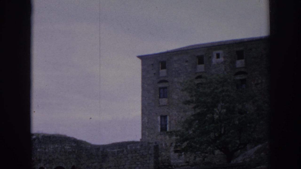 End frame from the 1966 Spain 8mm clip showing the stone parador facade, partial windows, a tree, and low surrounding wall.