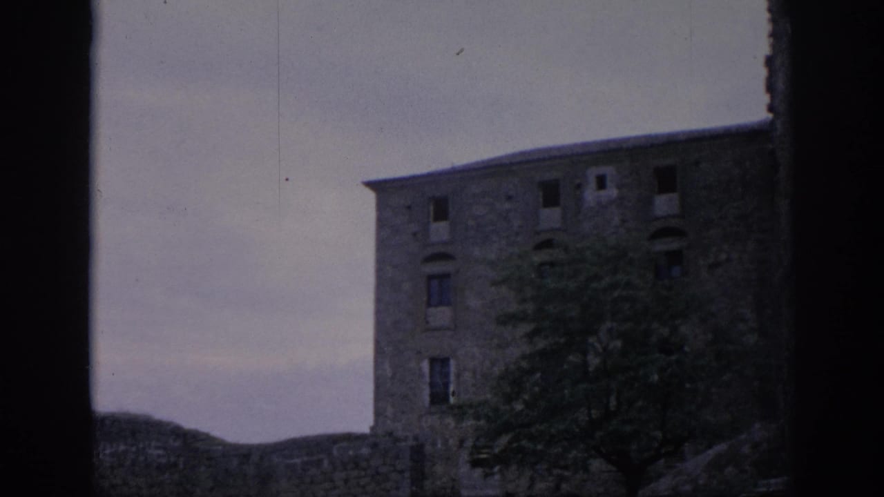 1966 Spain 8mm frame showing a weathered stone building through a dark foreground edge, with trees partly covering the lower facade.
