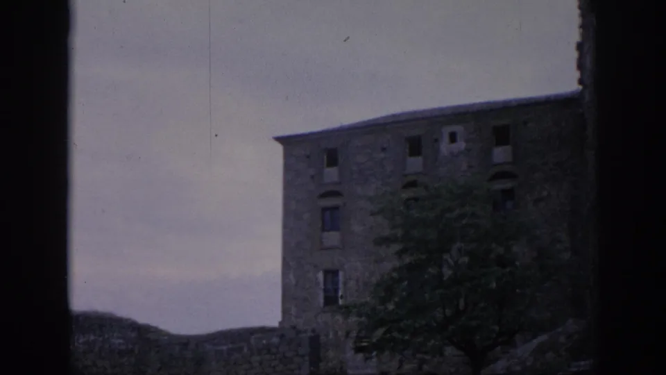 1966 Spain 8mm frame showing a weathered stone building through a dark foreground edge, with trees partly covering the lower facade.