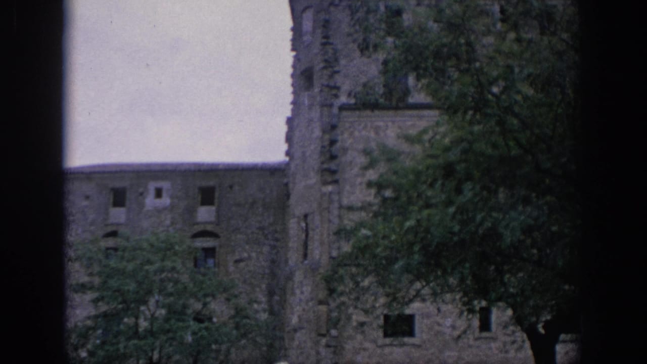 1966 Spain 8mm frame showing a weathered stone castle-like facade with small openings, tree cover, and dark scan borders.