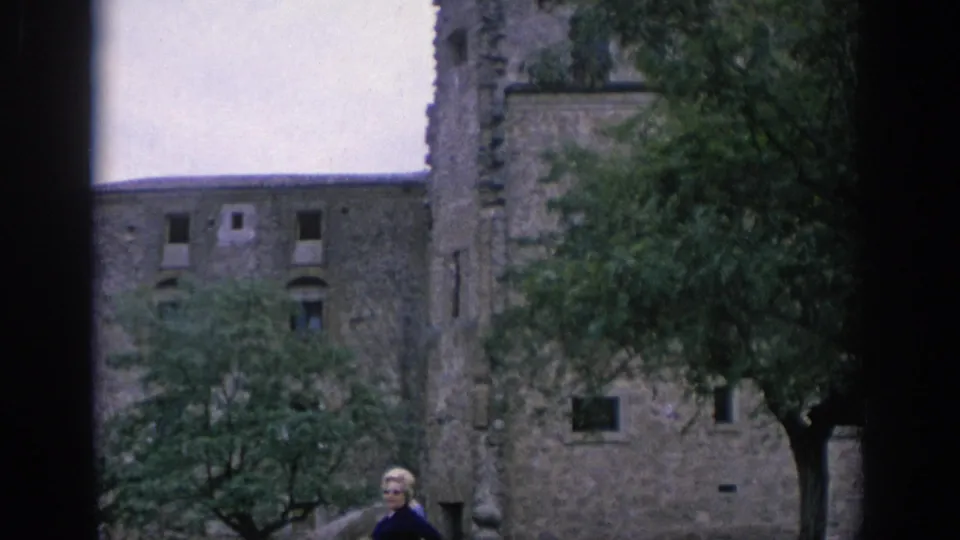 1966 Spain frame of a stone fortress-like exterior with trees, small window openings, and a visible adult figure near the bottom.
