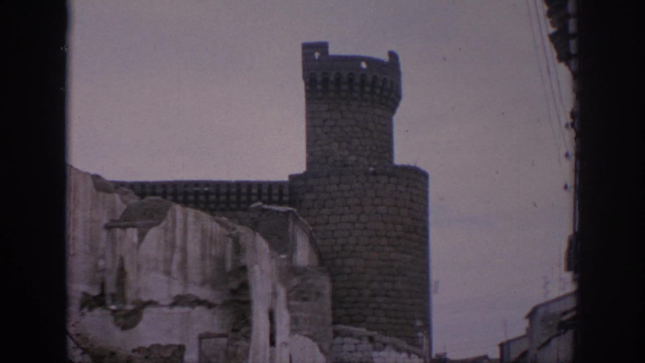 A 1966 Spain 8mm view of a castle tower and crenellated wall framed by rough, damaged masonry in the foreground.