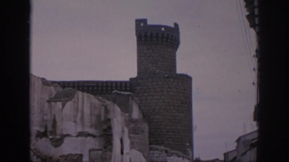 A 1966 Spain 8mm view of a castle tower and crenellated wall framed by rough, damaged masonry in the foreground.