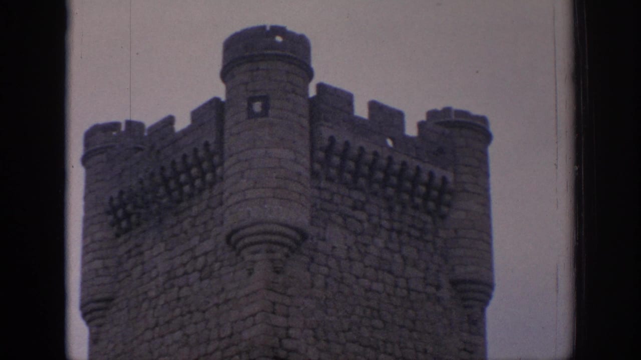 Close 1966 Spain home-movie view of a castle corner with rounded turrets, crenellations, and dark stone masonry.