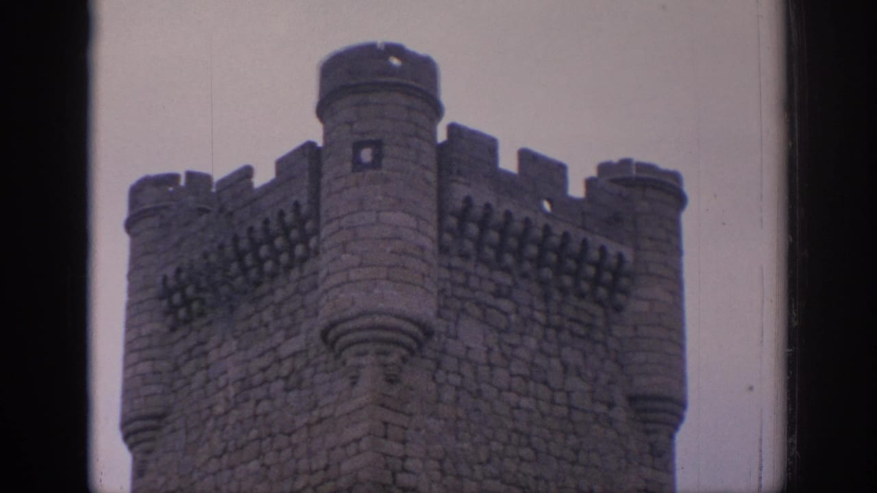A 1966 Spain 8mm frame of the castle's crenellated corner and rounded turrets, softened by faded color and film grain.