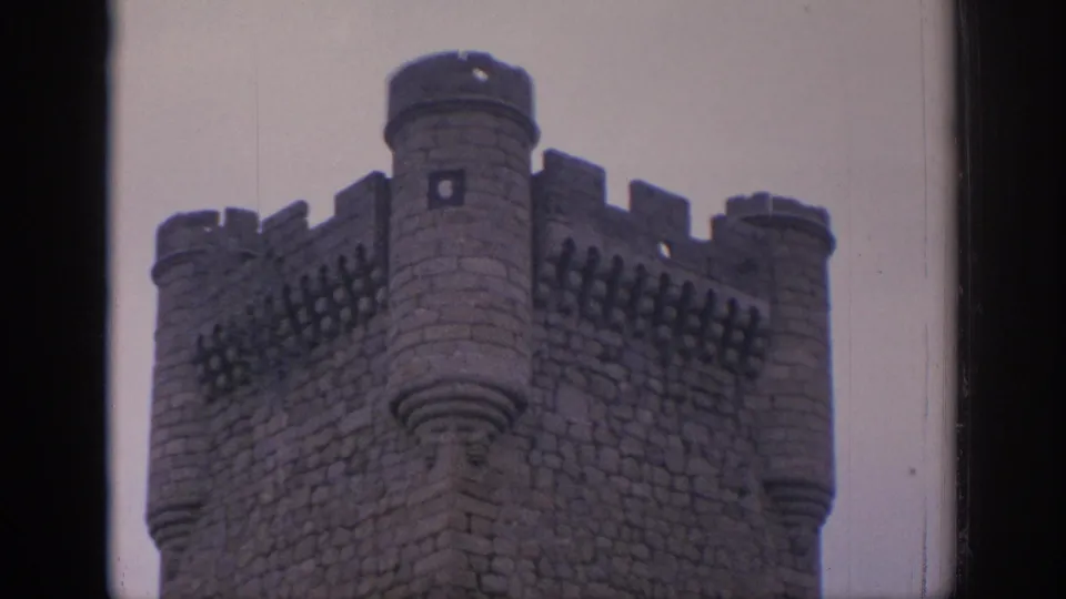 A 1966 Spain 8mm frame of the castle's crenellated corner and rounded turrets, softened by faded color and film grain.