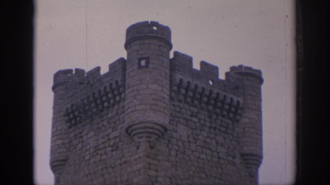 1966 Spain 8mm frame showing a crenellated stone castle tower and rounded turrets viewed through a dark architectural opening.