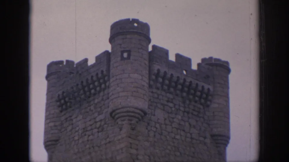 1966 Spain 8mm frame showing a crenellated stone castle tower and rounded turrets viewed through a dark architectural opening.